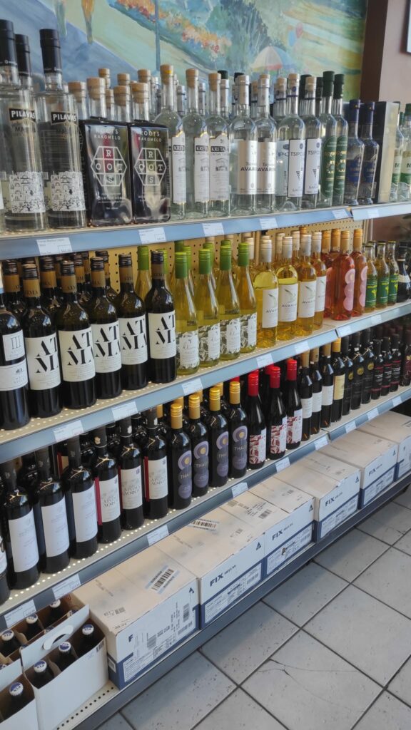Image of a retail store shelf with three shelf full of colourful bottled greek wines.