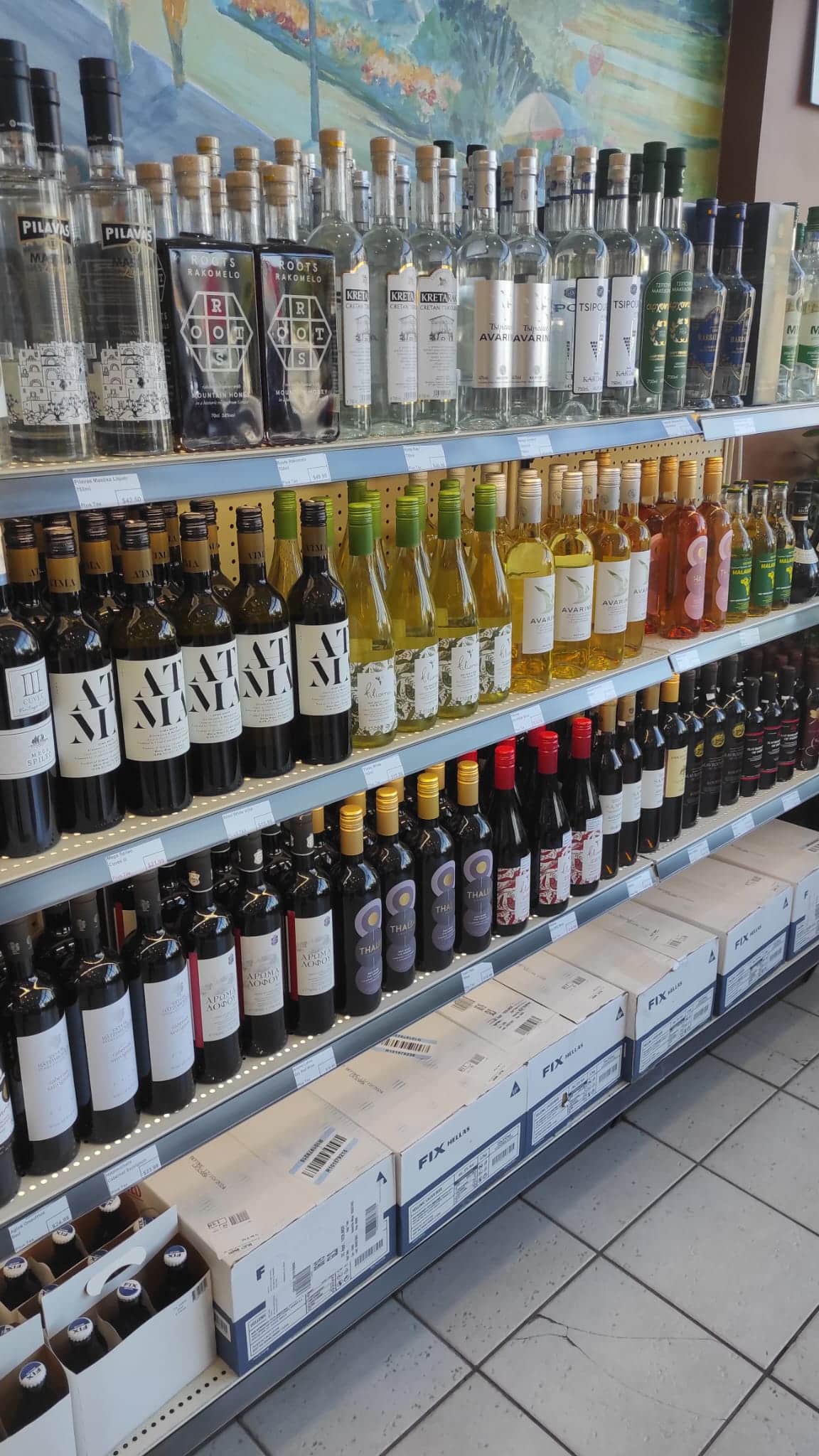 Image of a retail store shelf with three shelf full of colourful bottled greek wines.